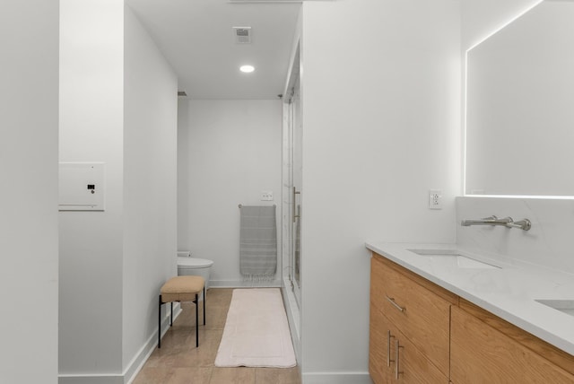 bathroom featuring baseboards, double vanity, a stall shower, toilet, and a sink