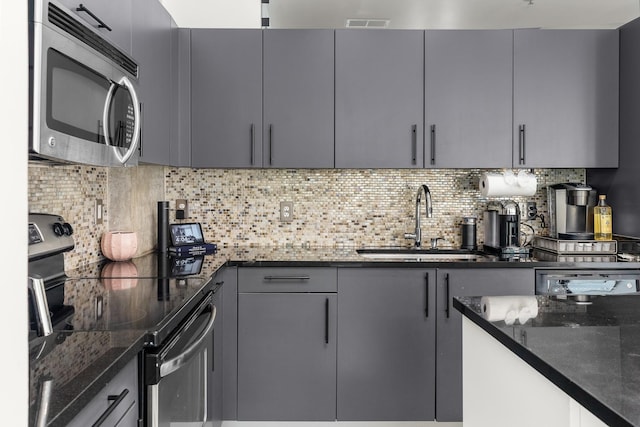 kitchen featuring dark stone counters, appliances with stainless steel finishes, a sink, decorative backsplash, and gray cabinetry