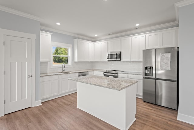 kitchen featuring crown molding, white cabinets, a kitchen island, appliances with stainless steel finishes, and a sink