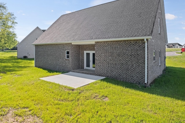back of house featuring a shingled roof, a yard, a patio area, brick siding, and french doors