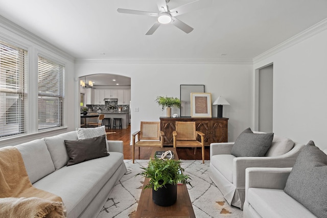 living room with arched walkways, light wood-style floors, crown molding, and a ceiling fan