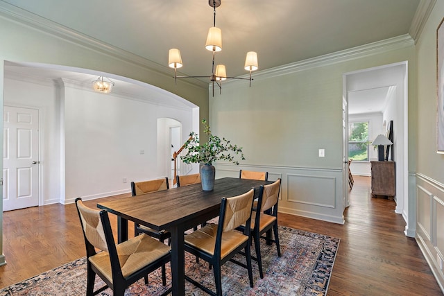 dining area featuring arched walkways, ornamental molding, a chandelier, wainscoting, and wood finished floors