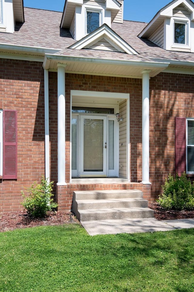 entrance to property with a lawn, brick siding, and roof with shingles