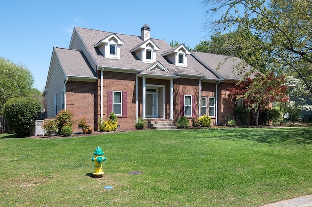 cape cod house featuring brick siding, roof with shingles, a chimney, and a front lawn