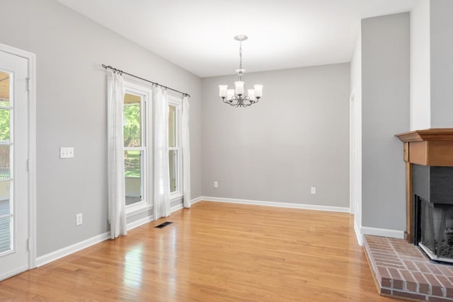 unfurnished dining area featuring a fireplace, light wood-style floors, visible vents, and a healthy amount of sunlight