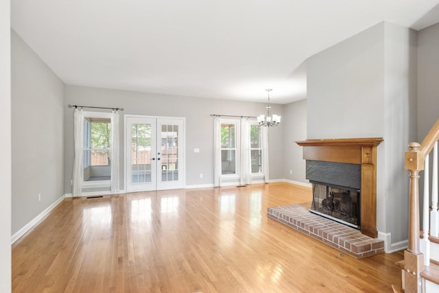 unfurnished living room with a fireplace, wood finished floors, a notable chandelier, and french doors