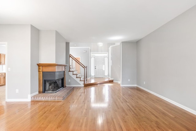 unfurnished living room with light wood-style floors, stairway, a brick fireplace, and baseboards