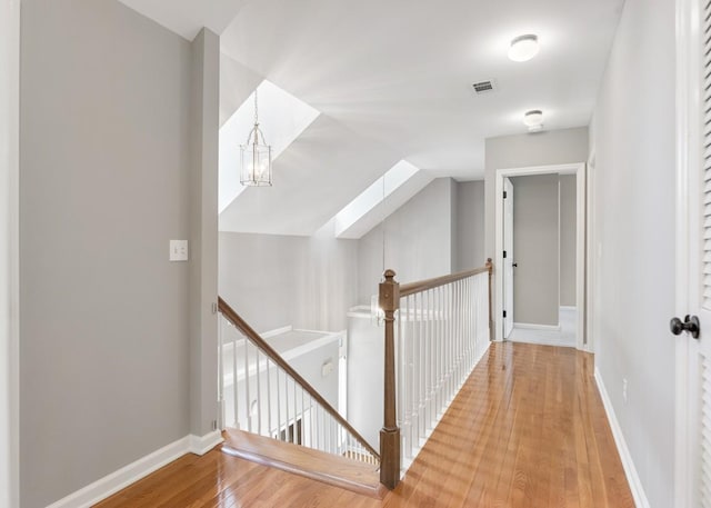 hall featuring wood finished floors, an upstairs landing, a skylight, baseboards, and visible vents