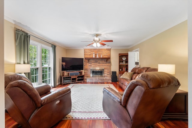 living area with a brick fireplace, ceiling fan, crown molding, and wood finished floors