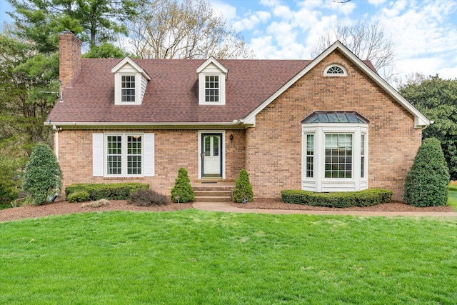 new england style home with a chimney, a shingled roof, a front yard, and brick siding
