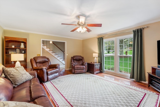 living room featuring ceiling fan, stairs, ornamental molding, and wood finished floors