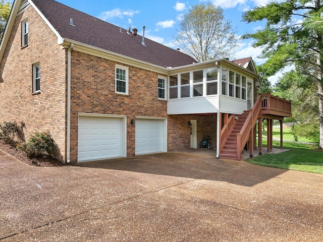 rear view of house featuring concrete driveway, stairway, an attached garage, brick siding, and a sunroom
