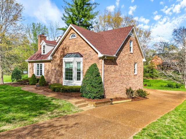 view of front of house with a chimney, a front lawn, brick siding, and a shingled roof