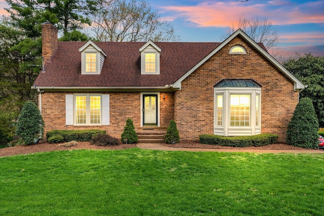 cape cod-style house with brick siding, a chimney, and a lawn