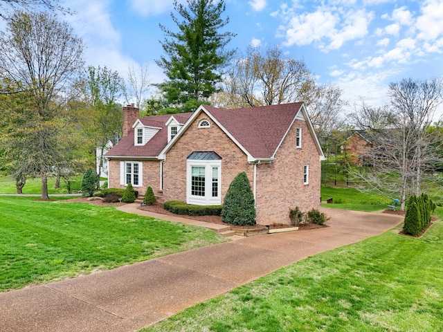 view of front of home with a front yard, a shingled roof, a chimney, brick siding, and driveway