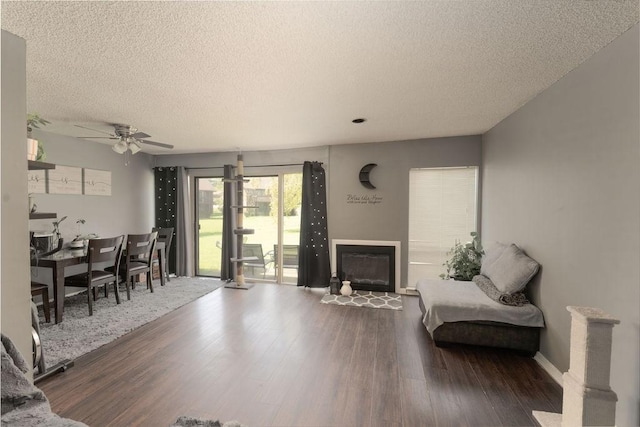 living area with ceiling fan, a textured ceiling, a glass covered fireplace, wood finished floors, and baseboards