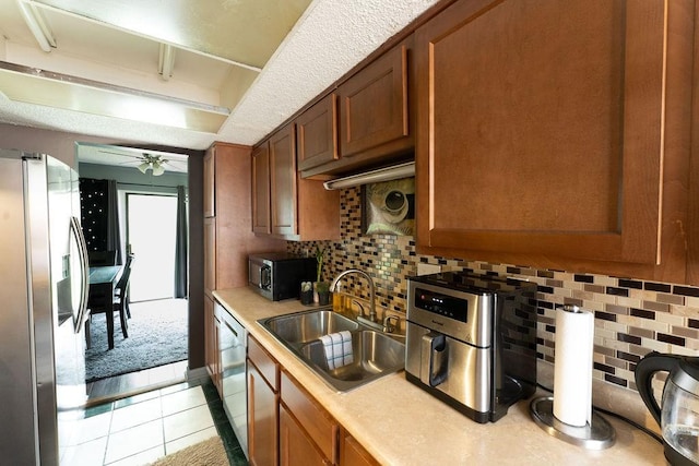 kitchen with ceiling fan, brown cabinetry, a sink, light countertops, and stainless steel appliances