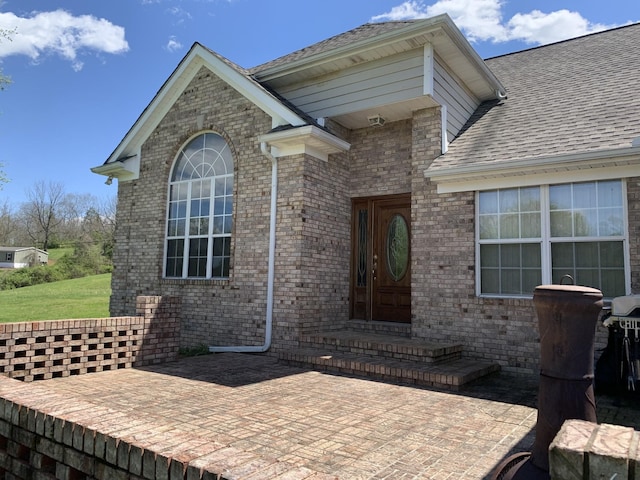 exterior space with brick siding, a shingled roof, and a yard