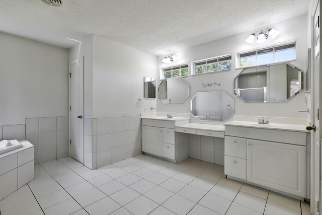 bathroom featuring two vanities, a sink, a textured ceiling, and tile walls