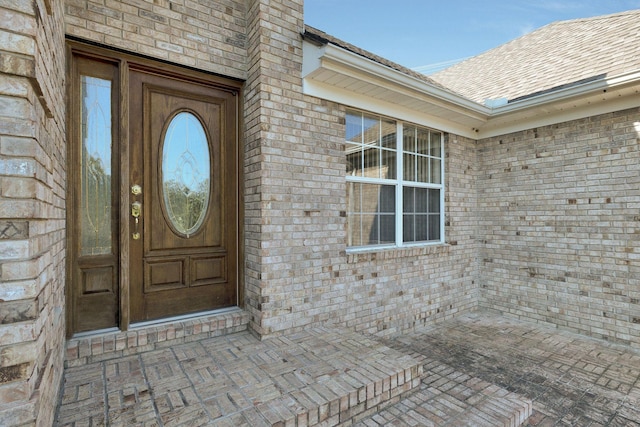 view of exterior entry featuring brick siding and roof with shingles