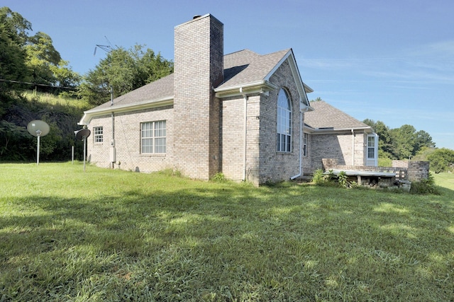 back of house with a yard, brick siding, a chimney, and a shingled roof