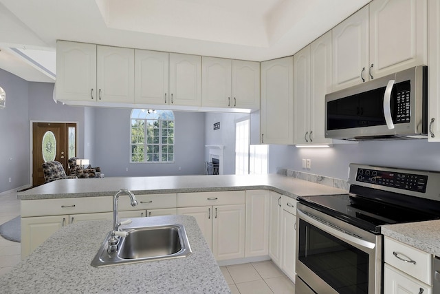 kitchen with a peninsula, appliances with stainless steel finishes, light tile patterned flooring, light countertops, and a sink