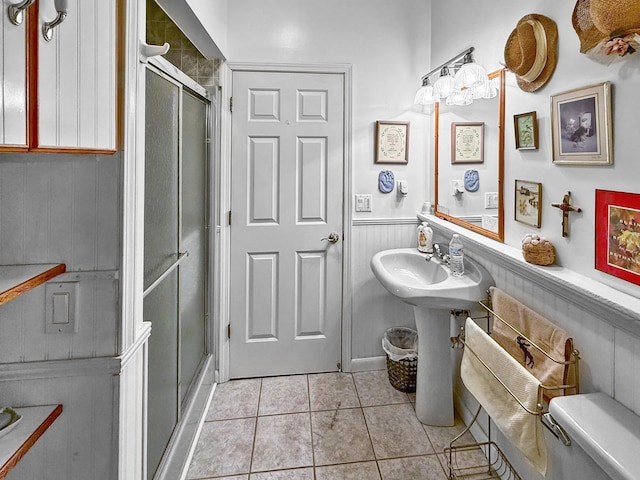 bathroom featuring a stall shower, tile patterned flooring, toilet, wainscoting, and a sink