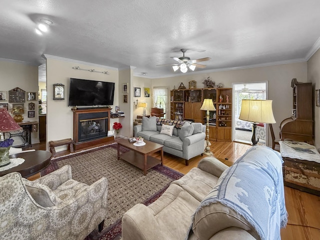 living area featuring a fireplace with raised hearth, ornamental molding, a ceiling fan, and wood finished floors