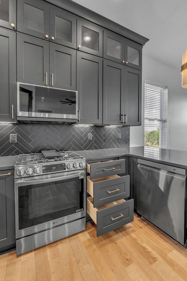418 Mercomatic Dr, Nashville, TN 37209 - kitchen featuring stainless steel appliances, light wood finished floors, dark countertops, gray cabinetry, and decorative backsplash