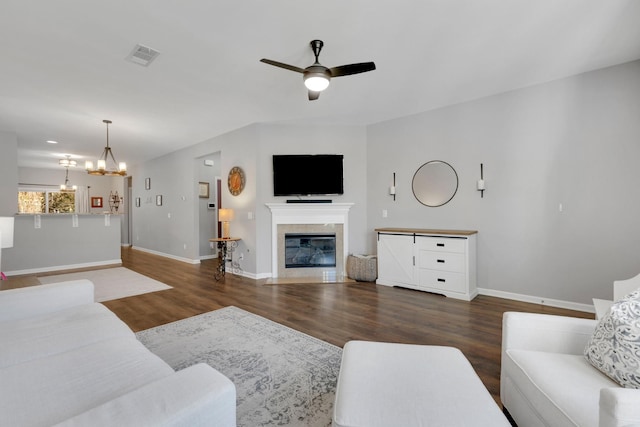 living area featuring a fireplace with flush hearth, baseboards, visible vents, ceiling fan with notable chandelier, and wood finished floors