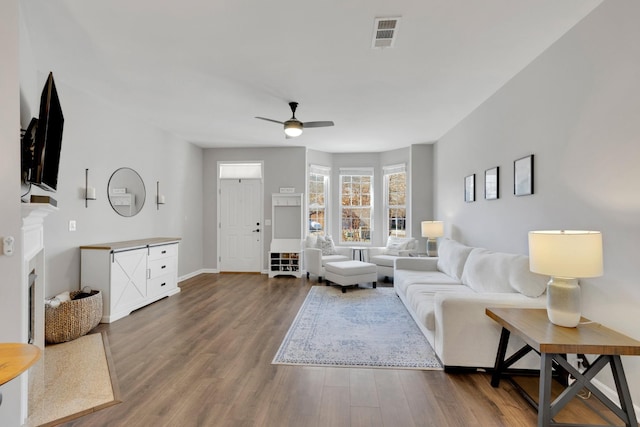 living area featuring visible vents, baseboards, a ceiling fan, and wood finished floors