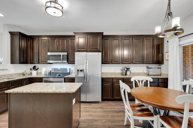 kitchen featuring light wood finished floors, a center island, dark brown cabinetry, hanging light fixtures, and appliances with stainless steel finishes