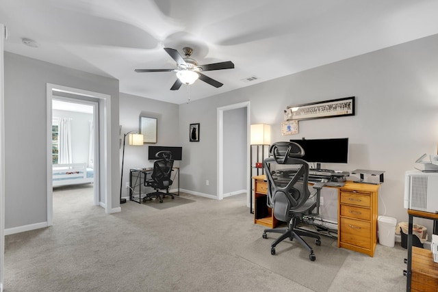 office space featuring light carpet, a ceiling fan, visible vents, and baseboards