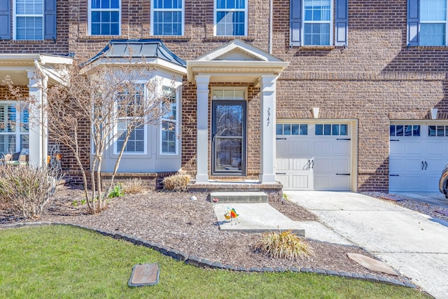 view of exterior entry with a garage, driveway, and brick siding