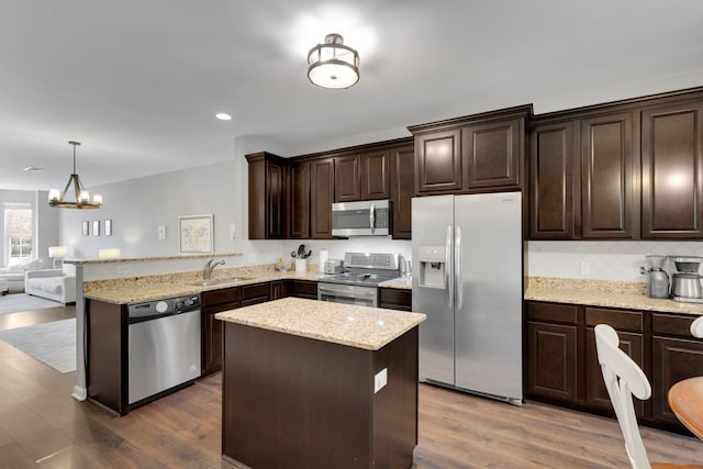 kitchen with stainless steel appliances, open floor plan, dark brown cabinetry, a notable chandelier, and light stone counters