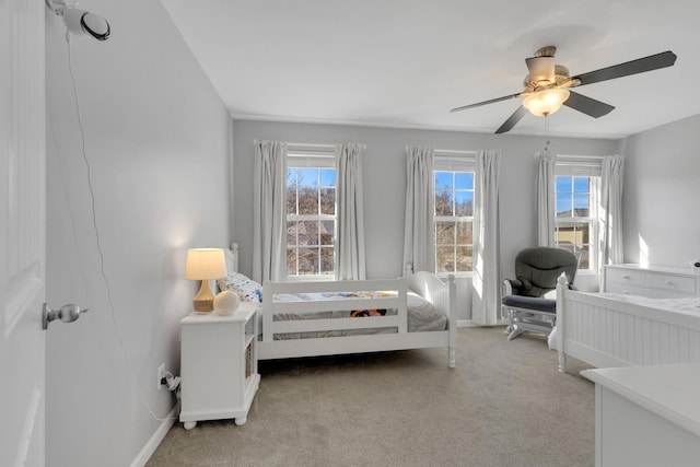 bedroom featuring ceiling fan, light carpet, multiple windows, and baseboards