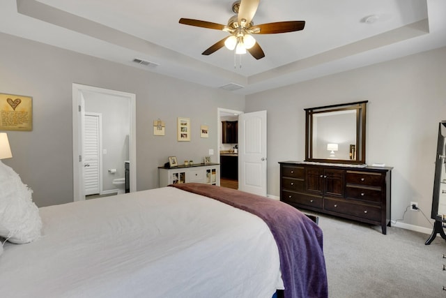 bedroom featuring a raised ceiling, visible vents, light carpet, baseboards, and ensuite bathroom