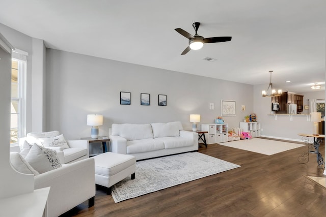 living area with ceiling fan with notable chandelier, baseboards, visible vents, and dark wood finished floors
