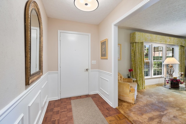 doorway to outside featuring a textured ceiling and wainscoting
