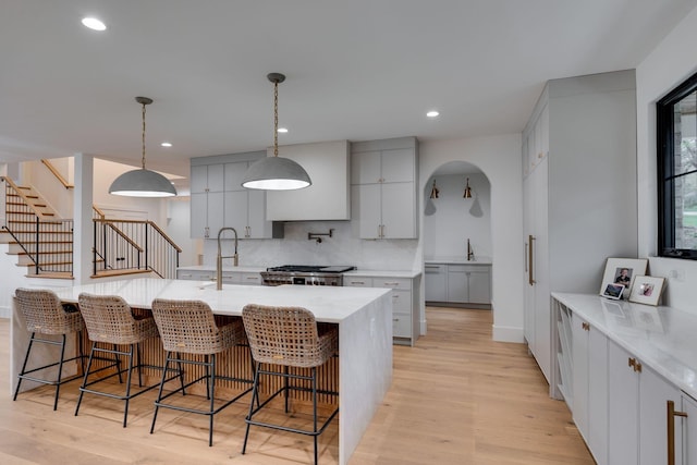 kitchen with a sink, a breakfast bar, light wood finished floors, backsplash, and stove