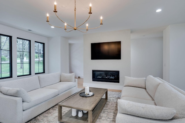 living area featuring recessed lighting, wood finished floors, visible vents, a glass covered fireplace, and a notable chandelier