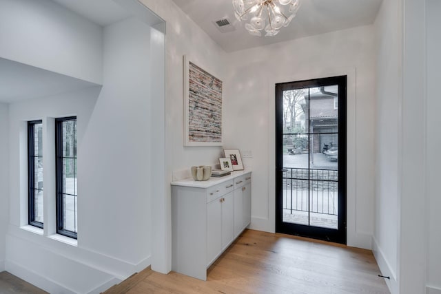 entryway featuring a wealth of natural light, a chandelier, visible vents, and light wood-style floors