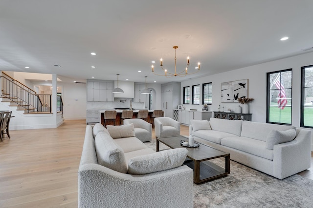 living area featuring stairs, an inviting chandelier, light wood finished floors, baseboards, and recessed lighting