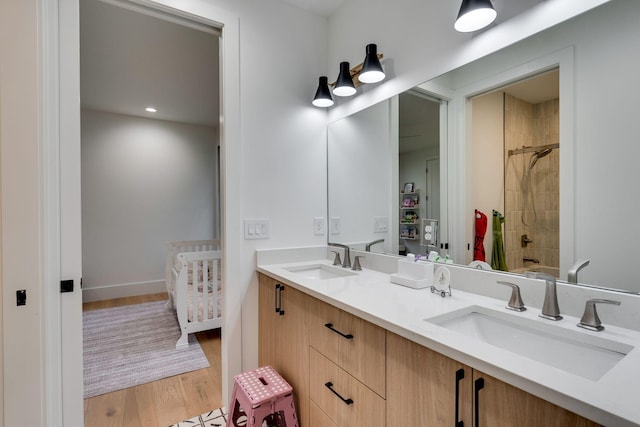 full bath featuring wood finished floors, a sink, double vanity, and tiled shower