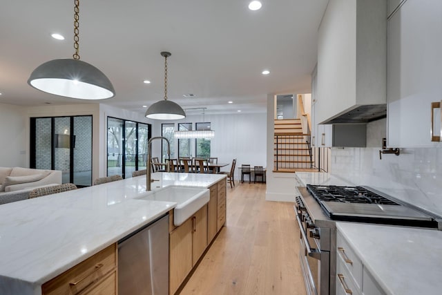 kitchen with light wood finished floors, stainless steel appliances, a sink, open floor plan, and custom exhaust hood