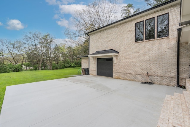 view of side of home with concrete driveway, an attached garage, a patio area, a lawn, and brick siding