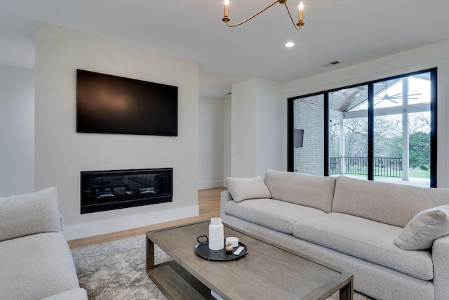 living room with a glass covered fireplace, baseboards, recessed lighting, a chandelier, and wood finished floors