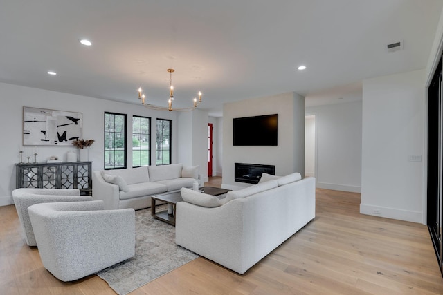 living area featuring recessed lighting, a glass covered fireplace, light wood-type flooring, and an inviting chandelier