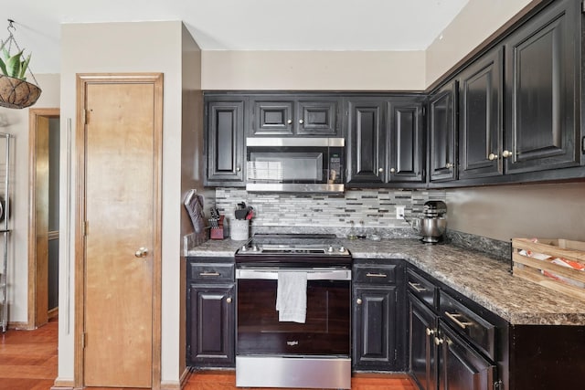 kitchen featuring dark cabinetry, decorative backsplash, light wood-style floors, and appliances with stainless steel finishes