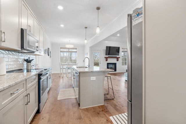 kitchen featuring stainless steel appliances, a sink, light wood-type flooring, decorative backsplash, and open floor plan